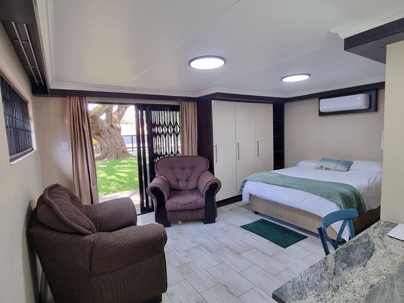 A well-maintained bedroom featuring built-in cupboards, tiled flooring, an air conditioning unit, and direct access to the garden through a sliding door.