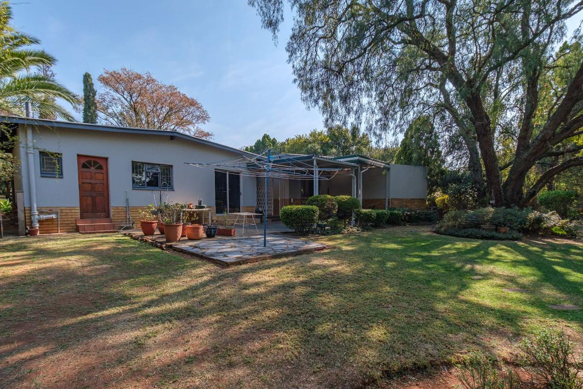 Rear view of the house featuring a stone paved patio, covered outdoor area, and a spacious garden with mature trees.