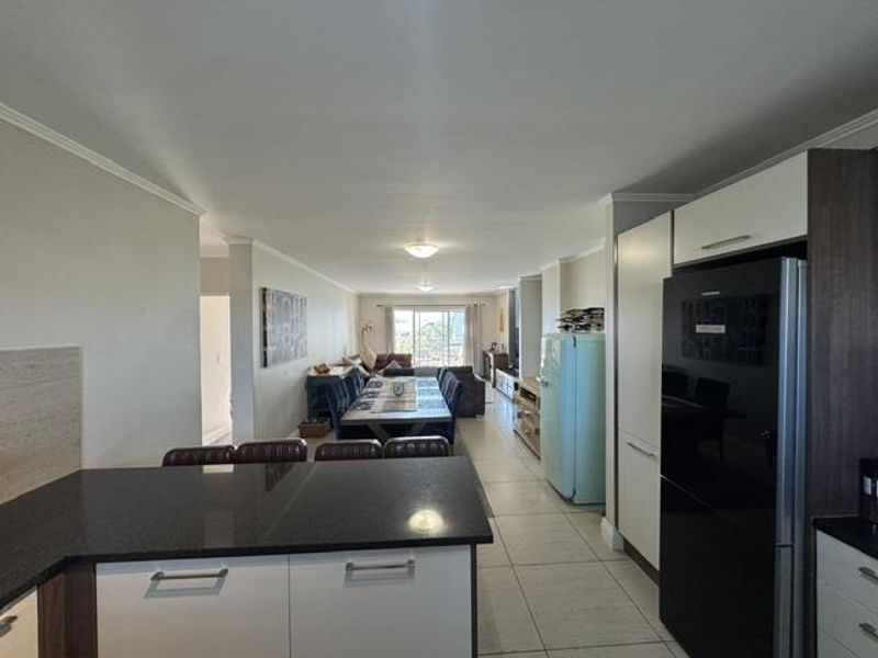 Spacious open-plan living and kitchen area featuring modern cabinetry, granite countertops, tiled flooring, and direct access to a balcony.