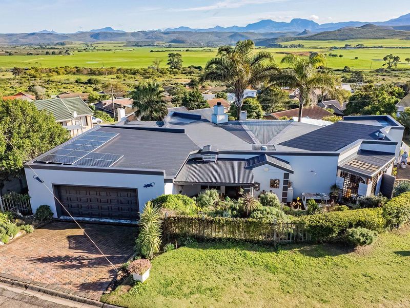 Aerial view of a well-maintained residential property featuring a metal roof with solar panels, a double garage, and expansive rural landscape views.