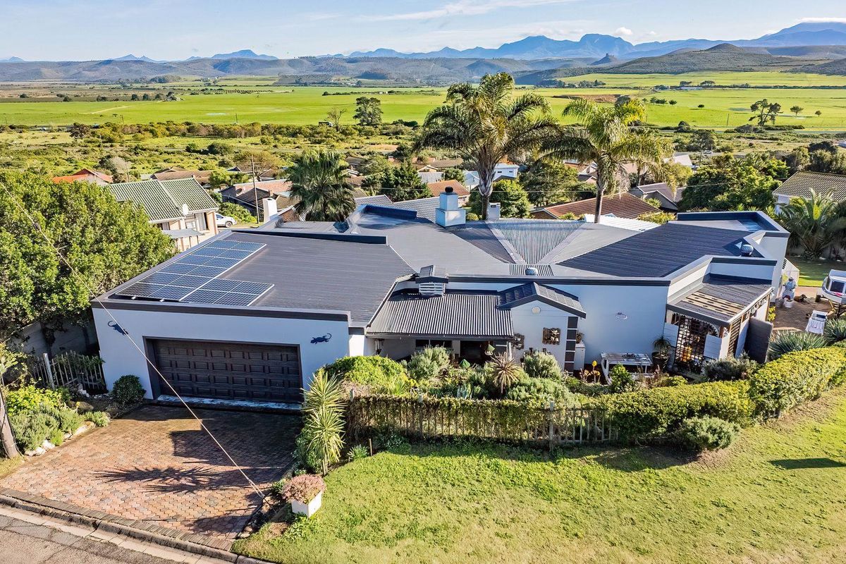 Aerial view of a well-maintained residential property featuring a metal roof with solar panels, a double garage, and expansive rural landscape views.
