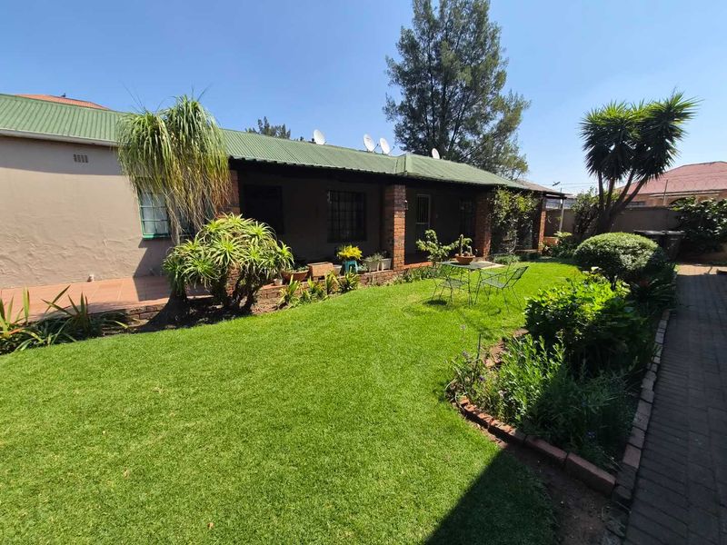 Rear view of the house featuring a covered patio, brick pillars, and a well-maintained garden with paved pathways.