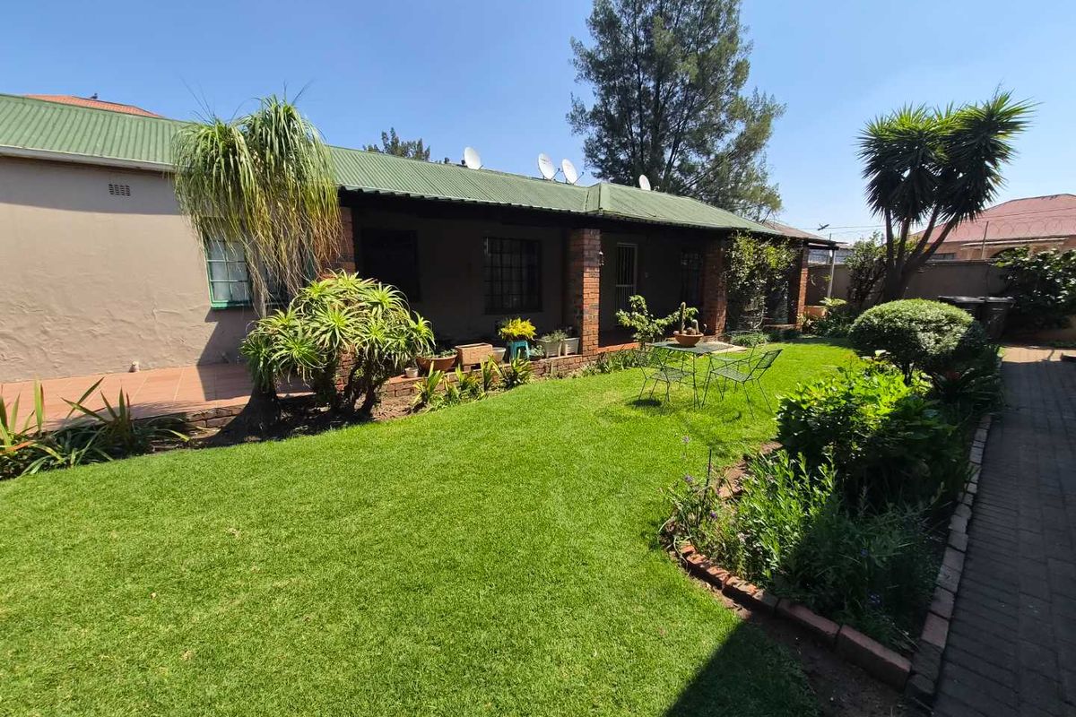Rear view of the house featuring a covered patio, brick pillars, and a well-maintained garden with paved pathways.