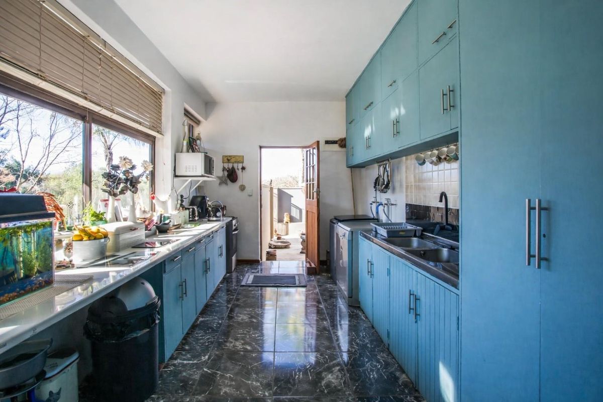 A functional galley-style kitchen featuring blue cabinetry, double stainless steel sink, tiled flooring, and direct access to the exterior.