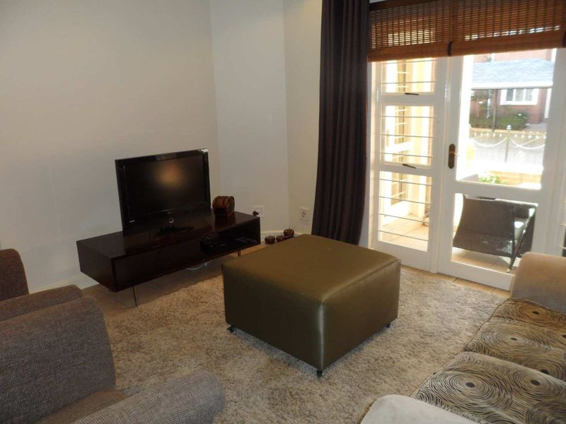 A living room featuring tiled flooring and a glass panel door leading to an outdoor area with a bamboo blind.