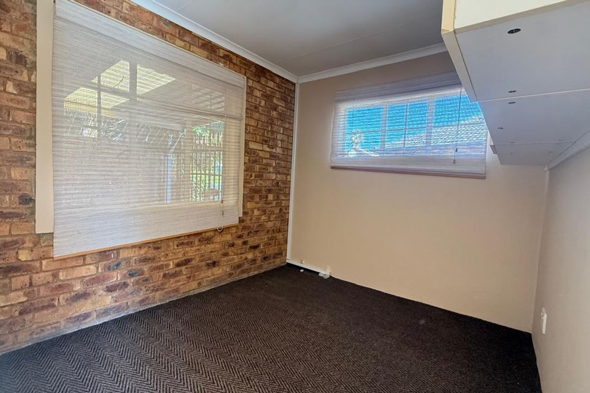 A bedroom featuring a distinctive exposed brick feature wall, neutral painted walls, and carpeted flooring with built-in shelving.