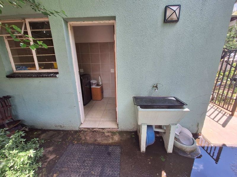 Exterior laundry area featuring a utility sink, tiled flooring, and wall-mounted lighting, showing signs of wear and external moisture.
