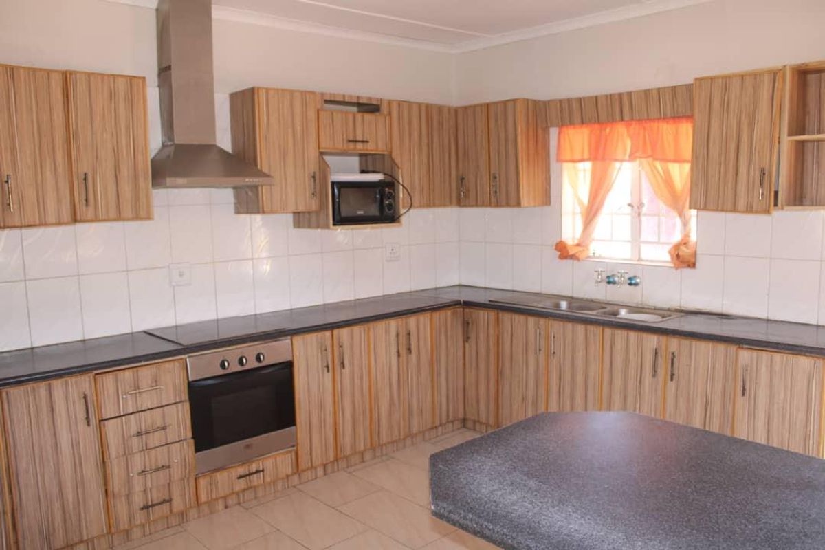 A functional kitchen featuring wood-look laminate cabinetry, built-in oven with extractor fan, double sink, and tiled backsplash.