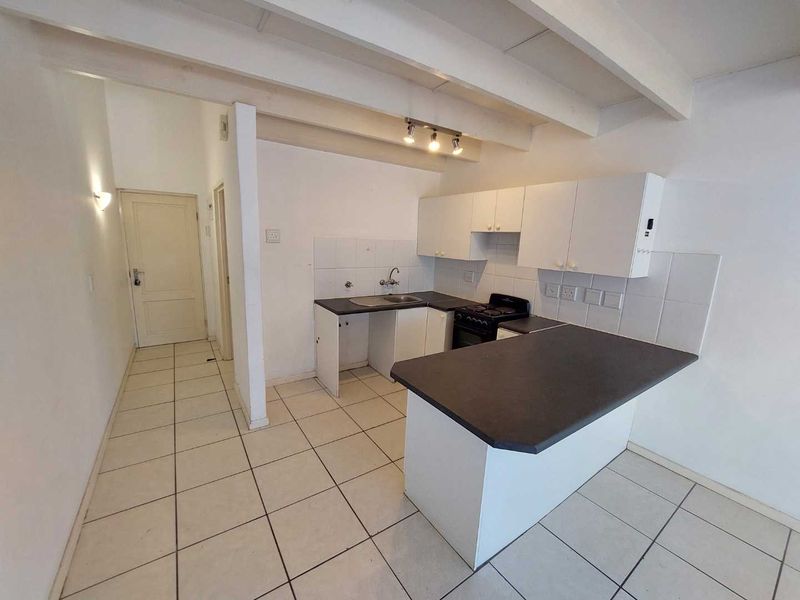 A functional kitchen featuring white cabinetry, dark countertops, tiled flooring, and exposed ceiling beams, offering a blank canvas for potential renovation.