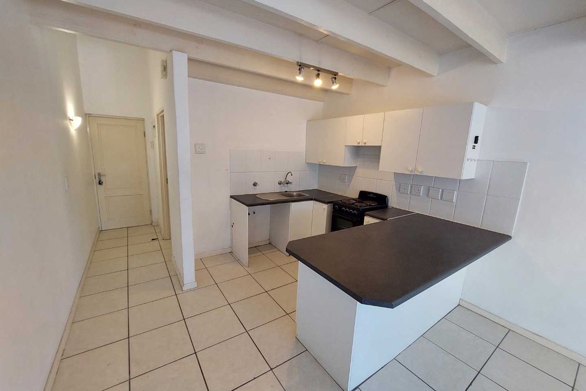 A functional kitchen featuring white cabinetry, dark countertops, tiled flooring, and exposed ceiling beams, offering a blank canvas for potential renovation.