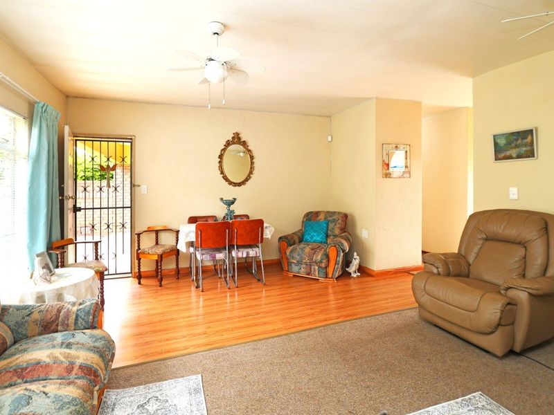Open plan living and dining area featuring a mix of laminate and carpet flooring, a ceiling fan, and direct access to an exterior security gate.