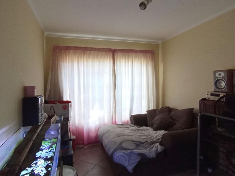 A living room area featuring tiled flooring and a large window with curtains, providing natural light to the space.