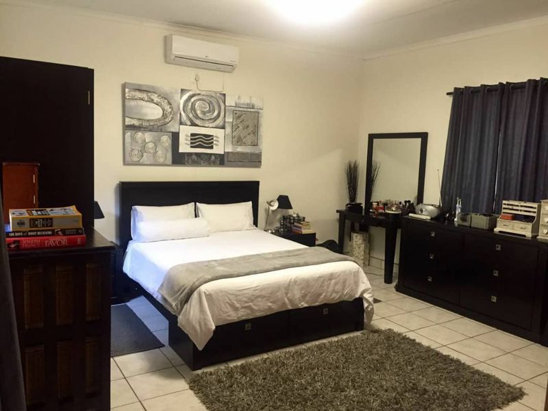 A spacious bedroom featuring tiled flooring and a wall-mounted air conditioning unit.