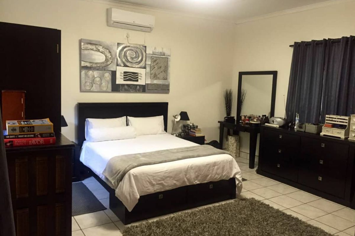 A spacious bedroom featuring tiled flooring and a wall-mounted air conditioning unit.