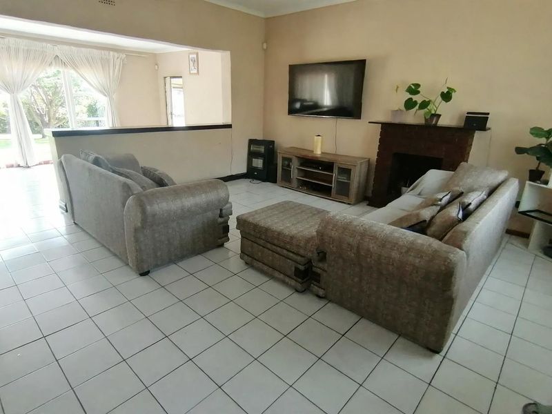 Spacious living room featuring tiled flooring, a brick fireplace, and an open-plan layout connecting to an adjacent area with large windows.