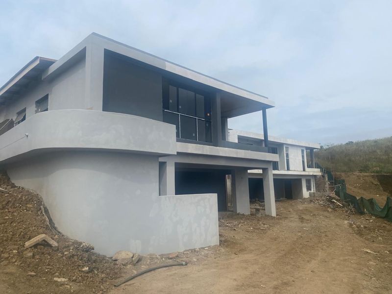 Rear view of a modern multi-story residential property under construction, featuring a curved retaining wall and upper-level balcony.
