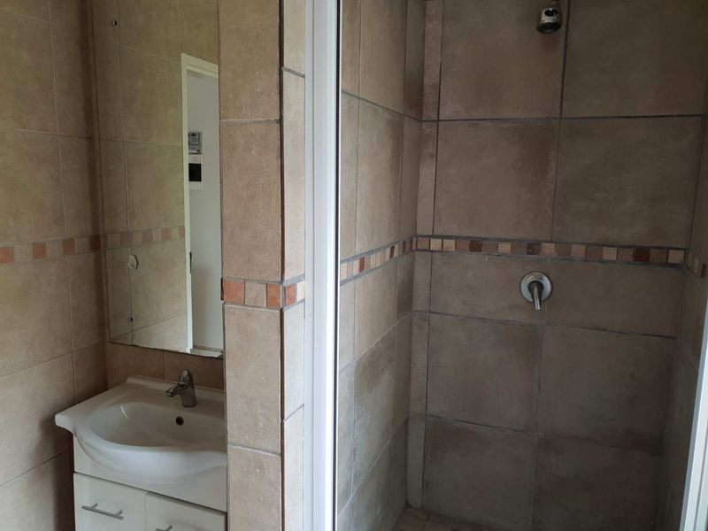 A functional bathroom featuring a tiled shower enclosure, a vanity cabinet with a basin, and wall-mounted mirror, finished with neutral ceramic wall tiles.