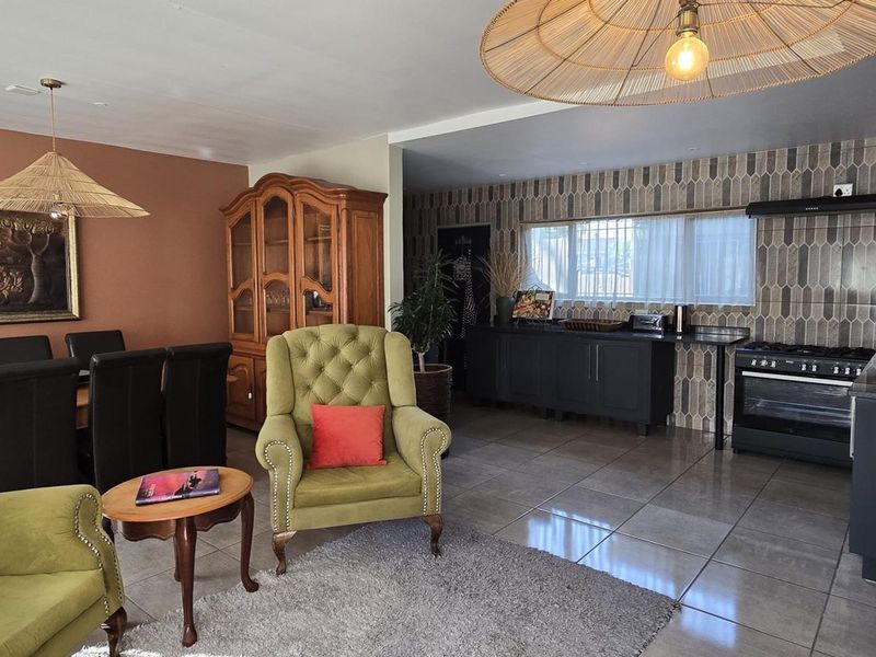 Spacious open-plan living and dining area featuring tiled floors, a modern kitchen with dark cabinetry, a gas stove, and a decorative tiled backsplash.