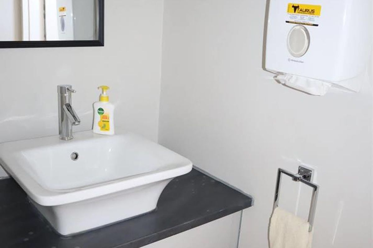 A functional office restroom featuring a modern vessel sink, dark countertop, vanity cabinet, wall-mounted paper towel dispenser, and a mirror.