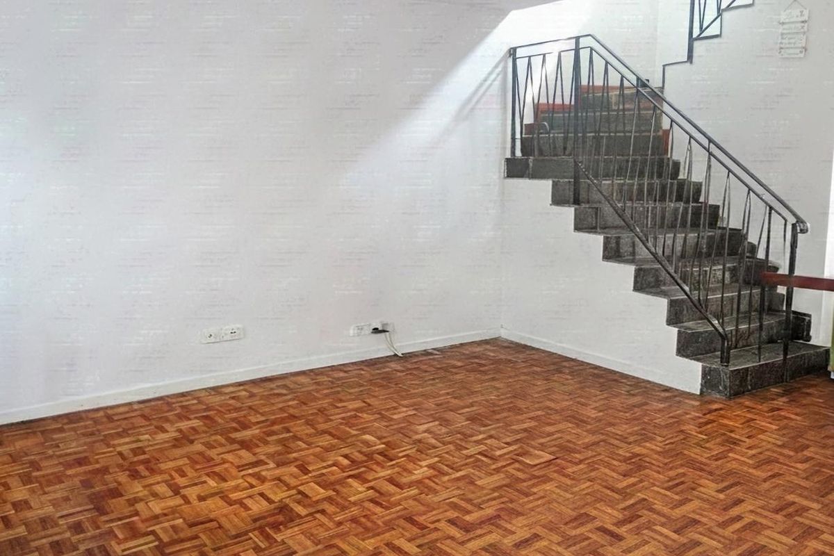 An empty living area featuring classic parquet flooring and a staircase with a metal balustrade, offering a blank canvas for interior design.