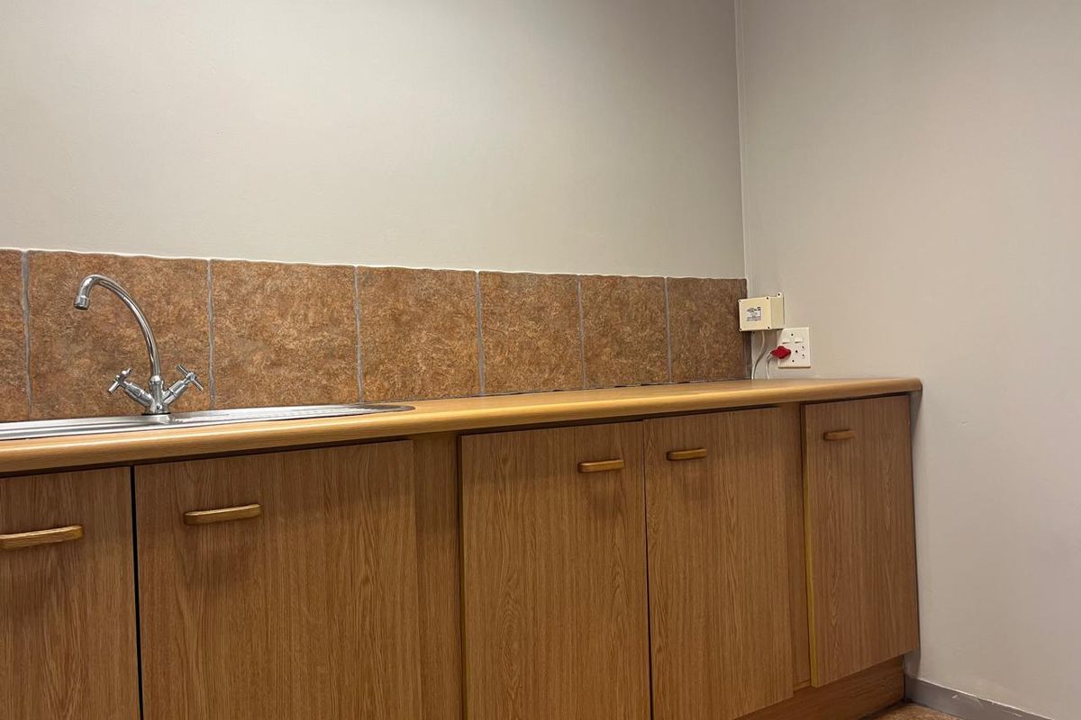 A functional office kitchenette featuring wood-grain cabinetry, a stainless steel sink, and a tiled backsplash.