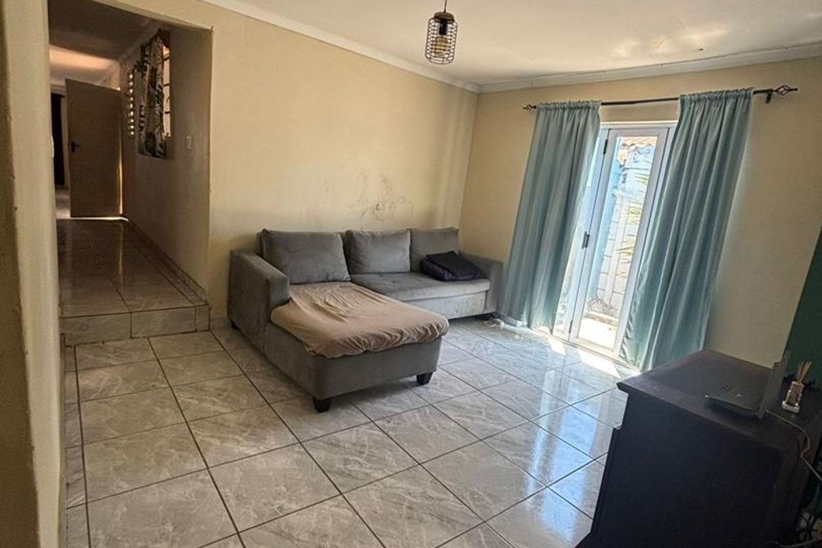A living room featuring tiled flooring, a pendant light fixture, and a glass door providing access to the exterior.