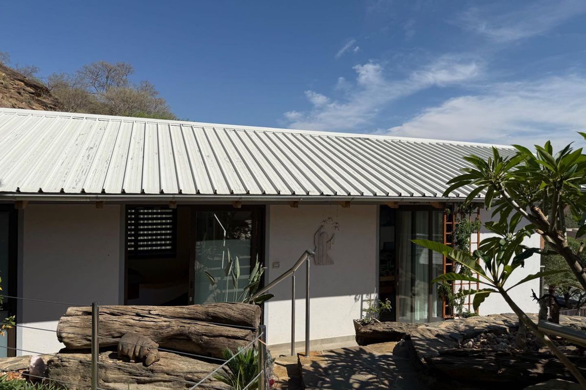 A view of the exterior rear facade featuring a corrugated metal roof, sliding glass doors, and a stone-paved pathway with stainless steel railings.