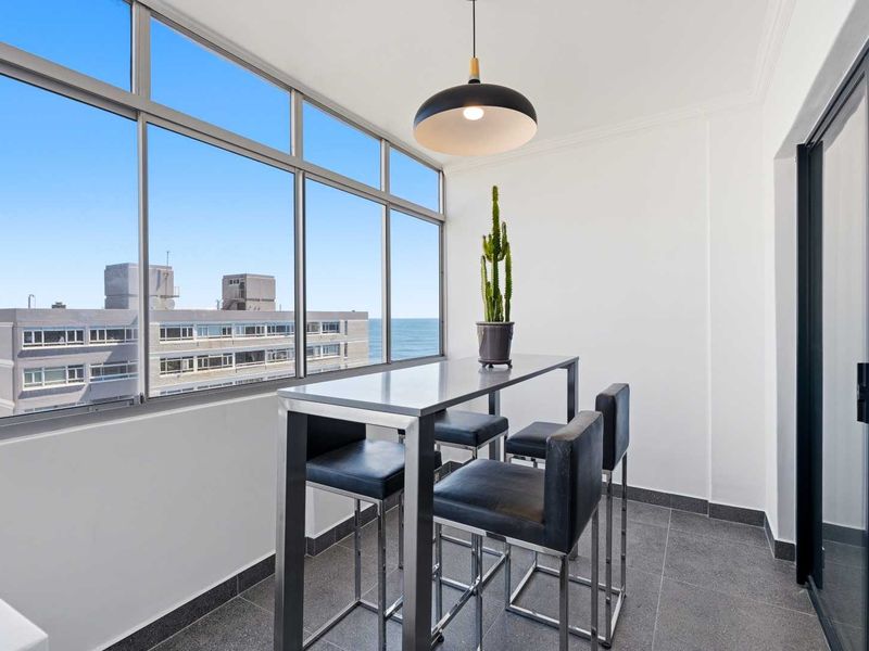 A bright, enclosed balcony featuring large windows with ocean views, tiled flooring, and a modern pendant light fixture.
