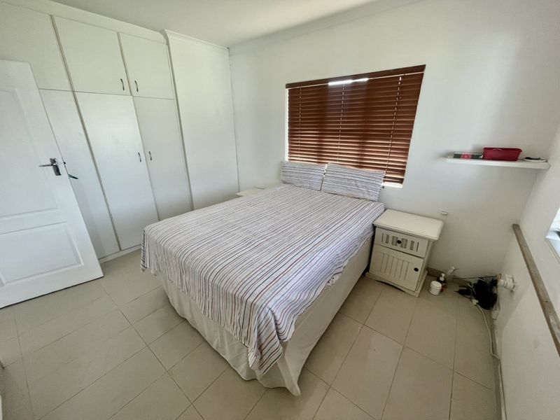 A functional bedroom featuring built-in cupboards, tiled flooring, and a window fitted with venetian blinds.