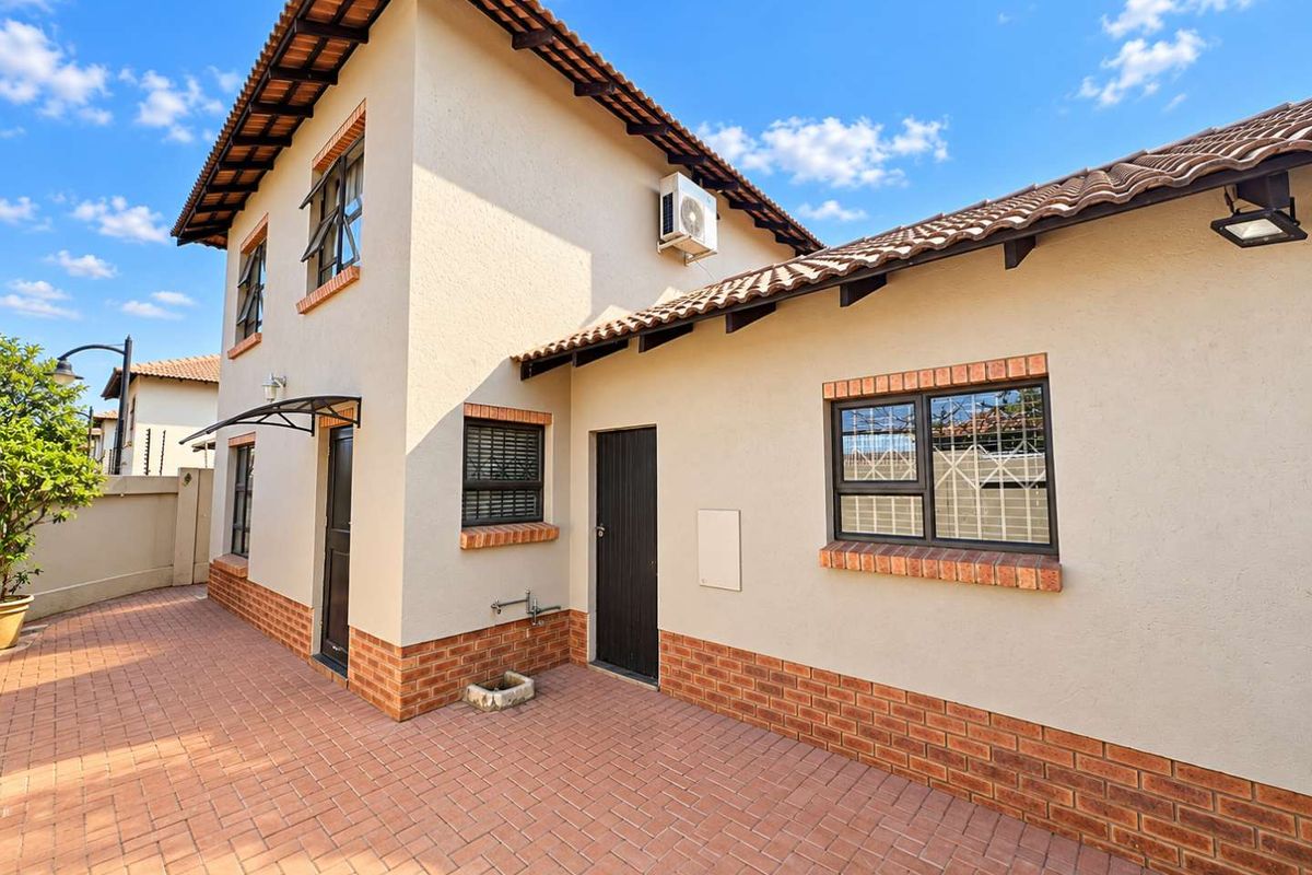 Rear exterior view of the townhouse featuring brick paving, a tiled roof, and secure window fittings with an installed air conditioning unit.
