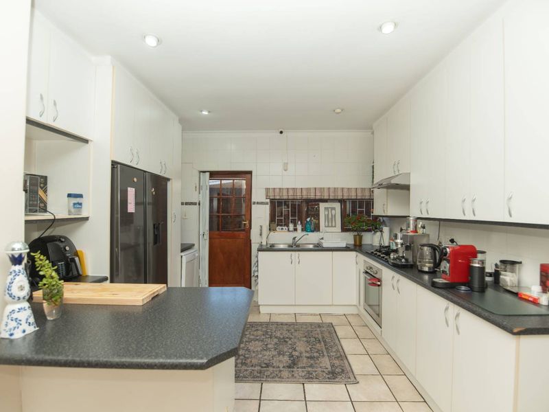 Functional kitchen featuring white cabinetry, dark laminate countertops, gas hob, built-in oven, and tiled flooring with direct access to the rear exterior.