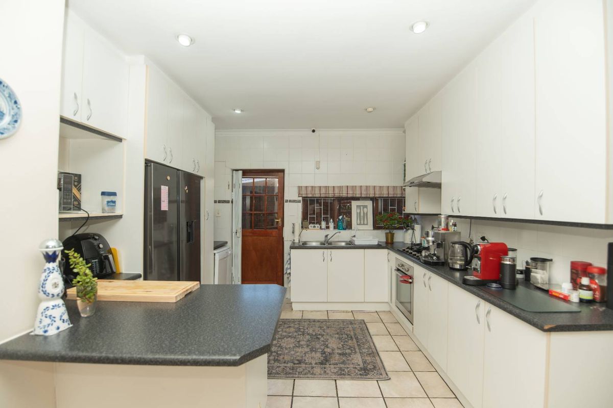 Functional kitchen featuring white cabinetry, dark laminate countertops, gas hob, built-in oven, and tiled flooring with direct access to the rear exterior.