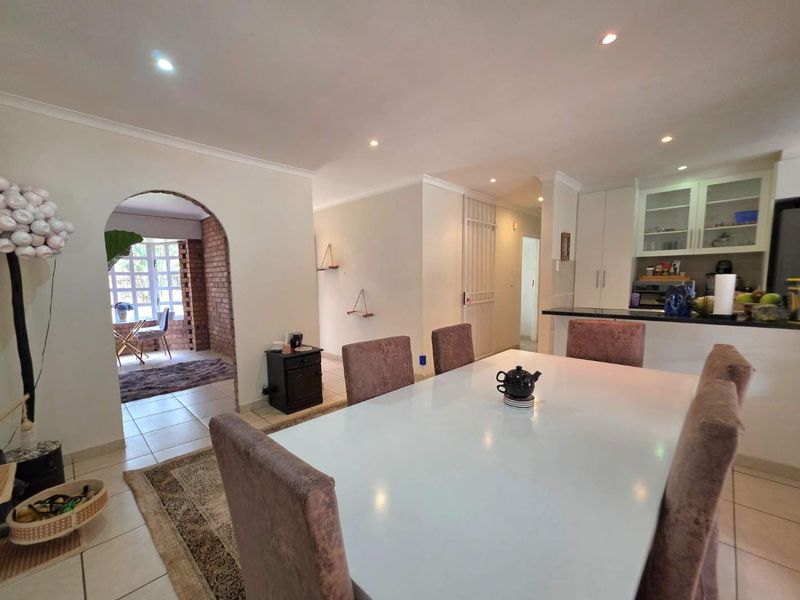 Open-plan dining area featuring tiled floors and recessed lighting, flowing into a kitchen with built-in cabinetry and a breakfast bar.