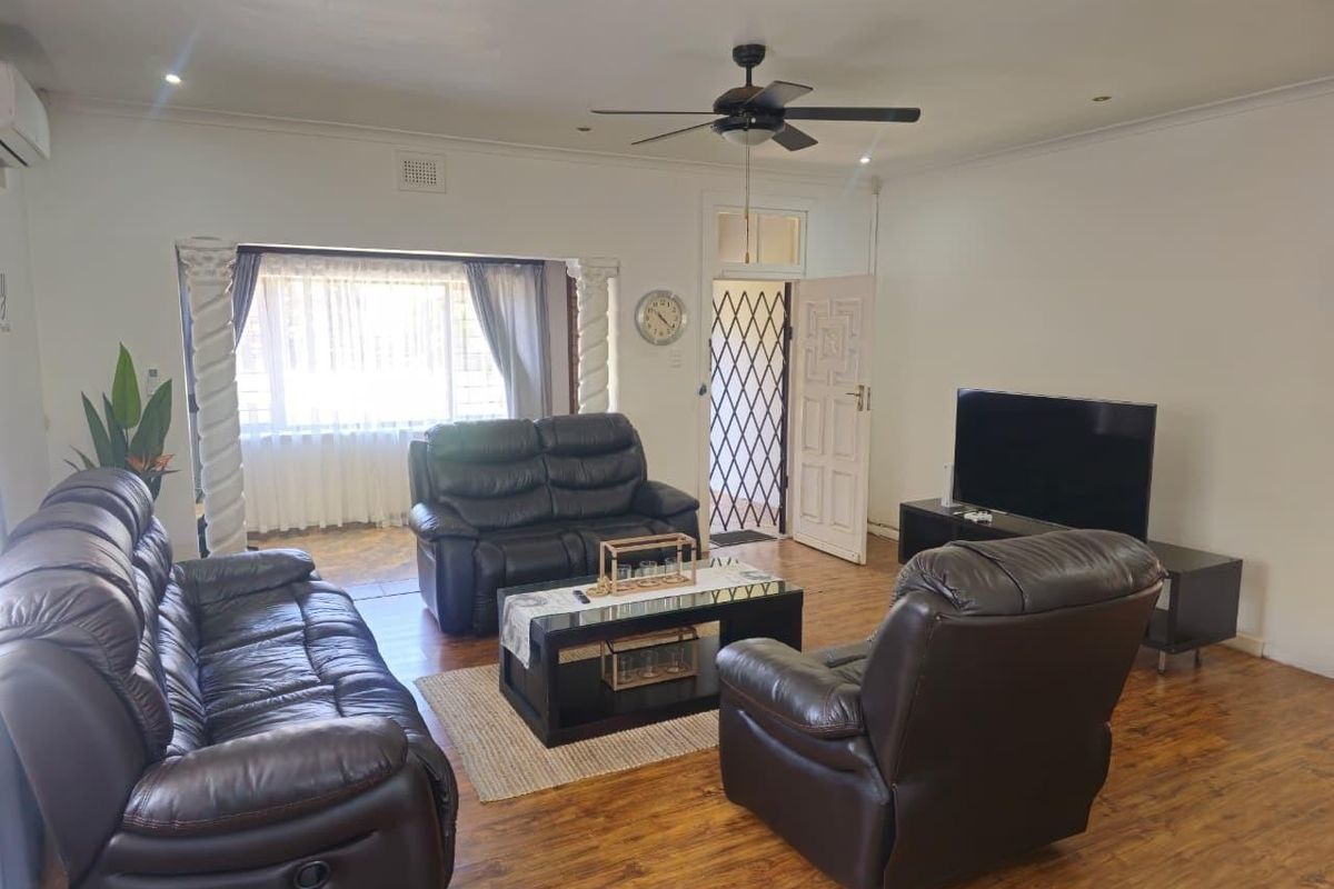 A spacious living room featuring laminate flooring, a ceiling fan, and decorative columns leading to an adjacent area with a security gate entrance.