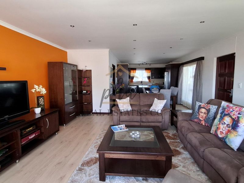 Open-plan living and kitchen area featuring laminate flooring, recessed downlighting, and a functional kitchen layout with built-in cabinetry and appliances.