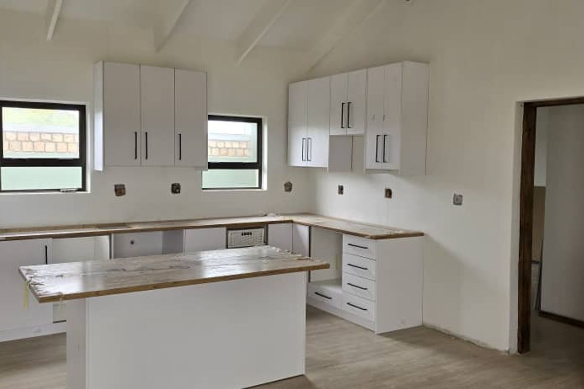 A modern kitchen featuring white cabinetry, wooden countertops, and a central island, currently undergoing final finishing touches.