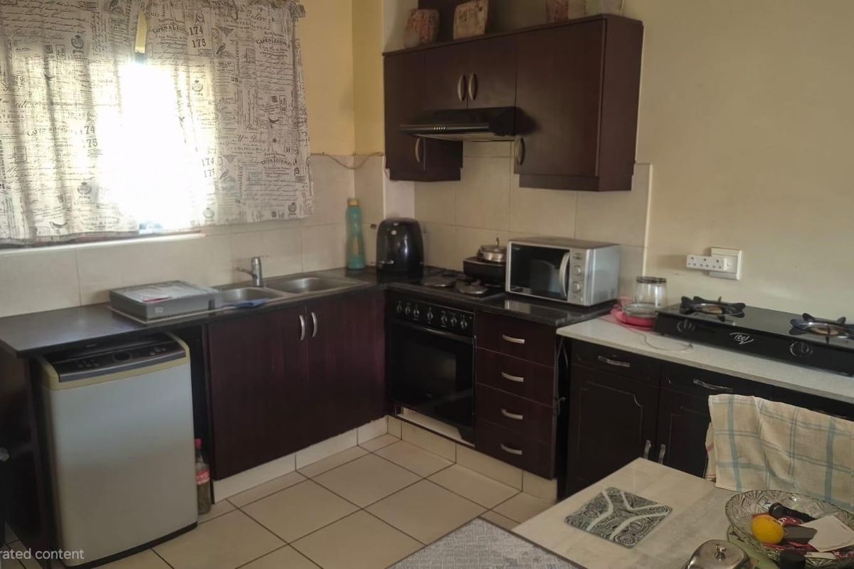 A functional kitchen featuring dark wood cabinetry, a built-in oven with extractor fan, double sink, and tiled flooring with a neutral backsplash.