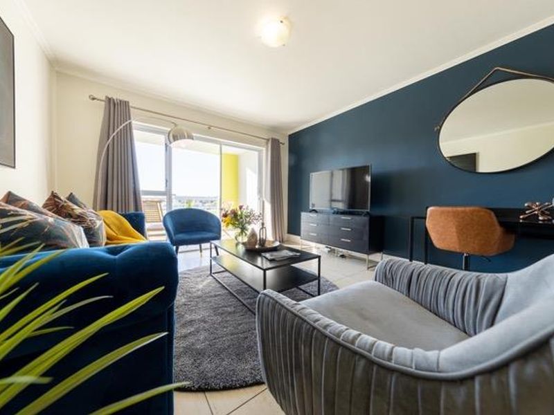 A well-lit living room featuring a bold navy accent wall, tiled flooring, and large sliding glass doors providing access to an outdoor area.