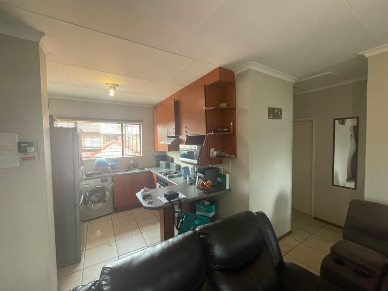 Open-plan kitchen and living area featuring tiled flooring, built-in cabinetry, and integrated appliances, offering a functional layout for modern apartment living.