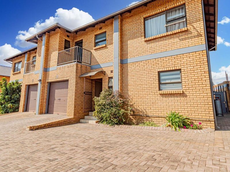 Front elevation of a double-storey townhouse featuring face brick construction, paved driveway, integrated garages, and a balcony.