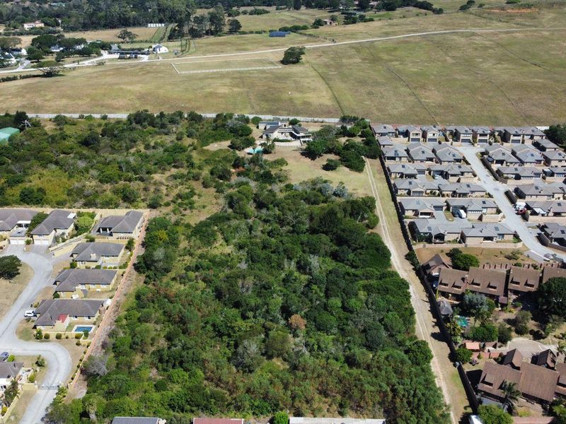 Aerial view of a vacant residential plot surrounded by established housing developments and natural vegetation.