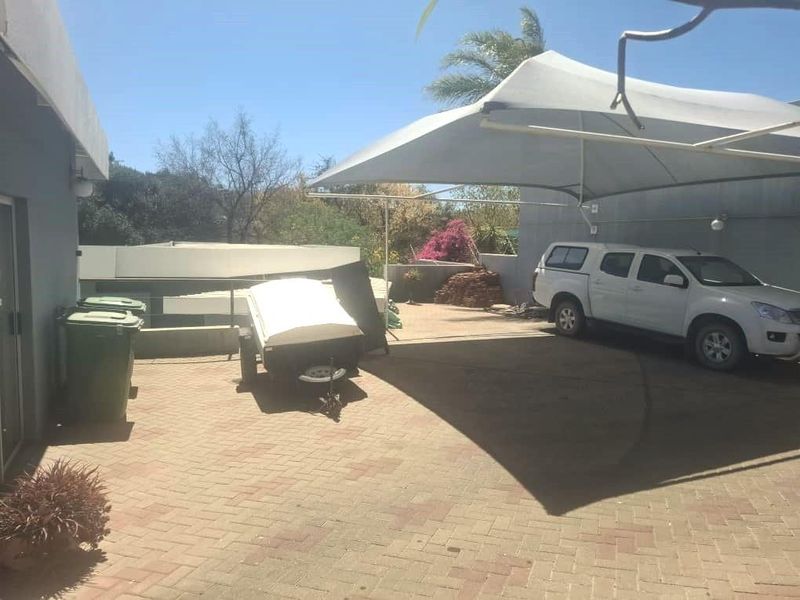 A paved driveway area featuring a large shade sail structure, providing covered parking space for vehicles.