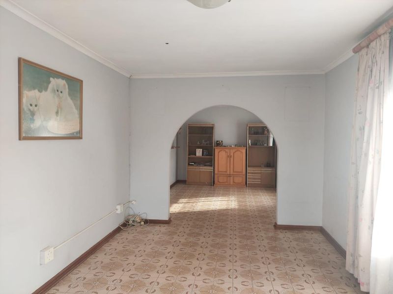 A spacious living area featuring a distinctive arched doorway, tiled flooring, and coved cornicing, offering a blank canvas for renovation.