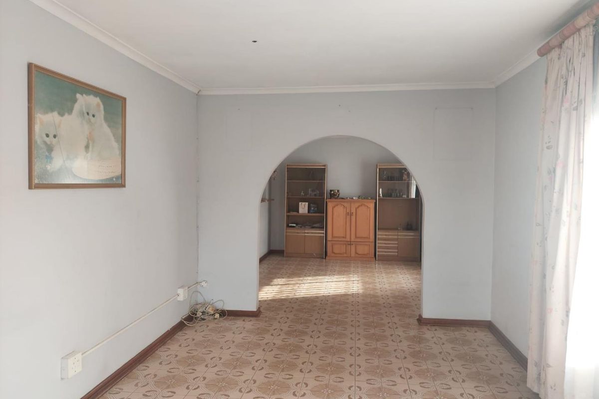 A spacious living area featuring a distinctive arched doorway, tiled flooring, and coved cornicing, offering a blank canvas for renovation.