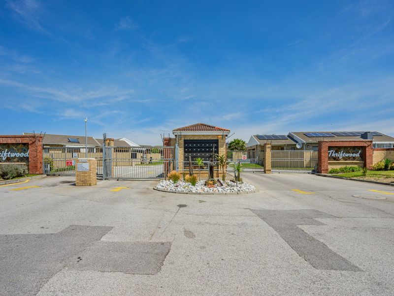 The secure entrance to Thriftwood complex featuring brick pillars, electric gates, integrated post boxes, and solar-equipped residential units.