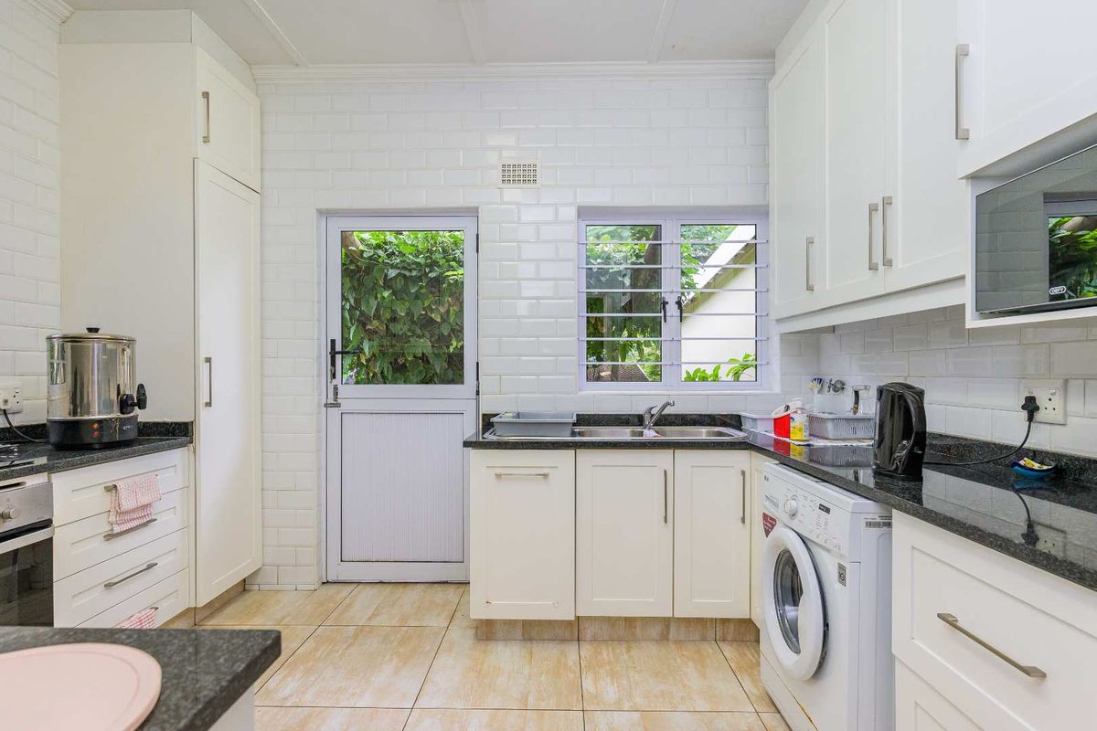 A functional kitchen featuring white cabinetry, dark granite countertops, subway tile backsplash, and integrated laundry plumbing.