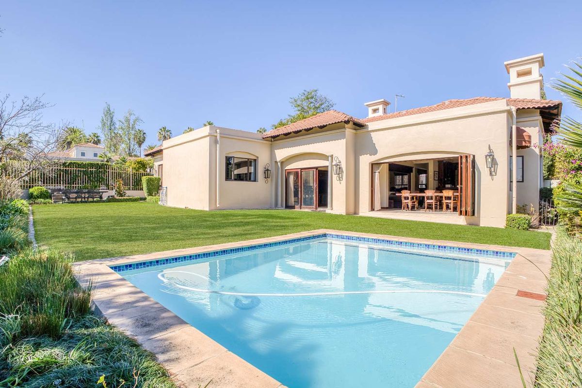 Rear view of the property featuring a well-maintained swimming pool, manicured lawn, and seamless indoor-outdoor flow through large bi-fold doors.