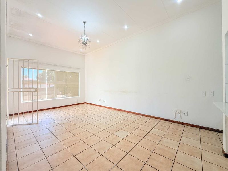 A spacious, empty living area featuring tiled flooring, recessed downlights, and a security gate, offering a blank canvas for personalization.