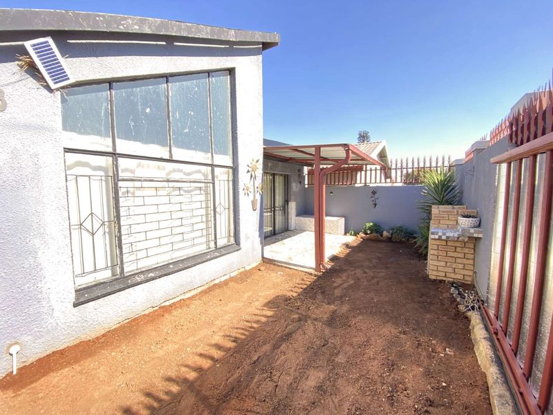 Rear exterior area featuring a covered patio, built-in braai, and an open garden space ready for landscaping.