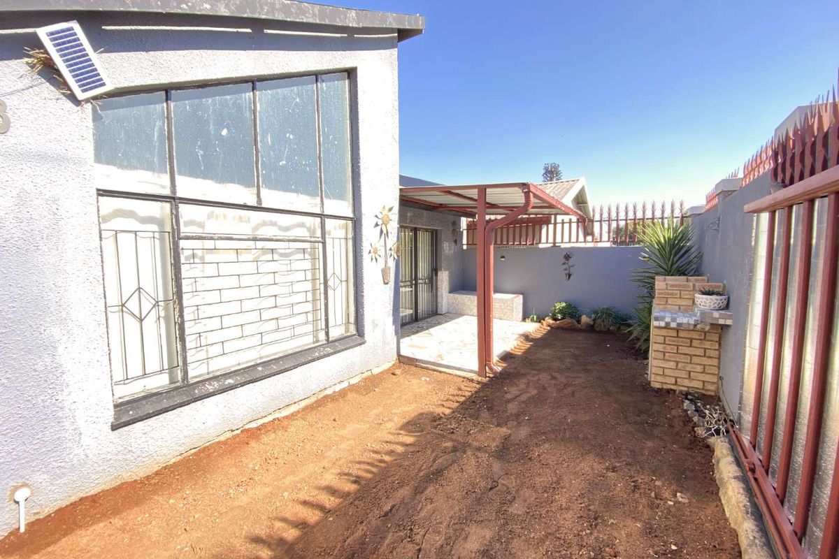Rear exterior area featuring a covered patio, built-in braai, and an open garden space ready for landscaping.
